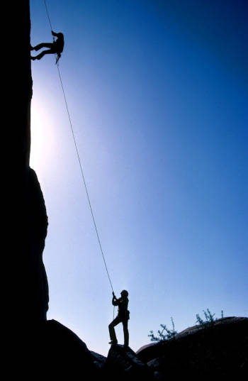 image d'un grimpeur sur une paroi rocheuse, guidé par un coach qui l'assure à l'aide d'une corde d'escalade