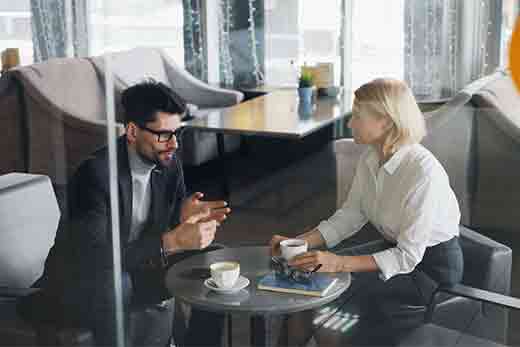 un homme et une femme autour d'une table avec un café échangent lors d'un entretien d'embauche