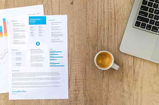 Une table avec, posé dessus, le formulaire d'un CV, un laptop et une tasse de café pour illustrer la préparation d'un CV