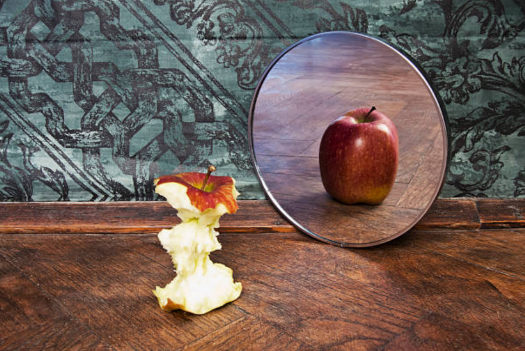 Au-delà de l'apparence Un miroir avec une pomme rognée devant. Dans le miroir c'est une pomme entière qui apparait